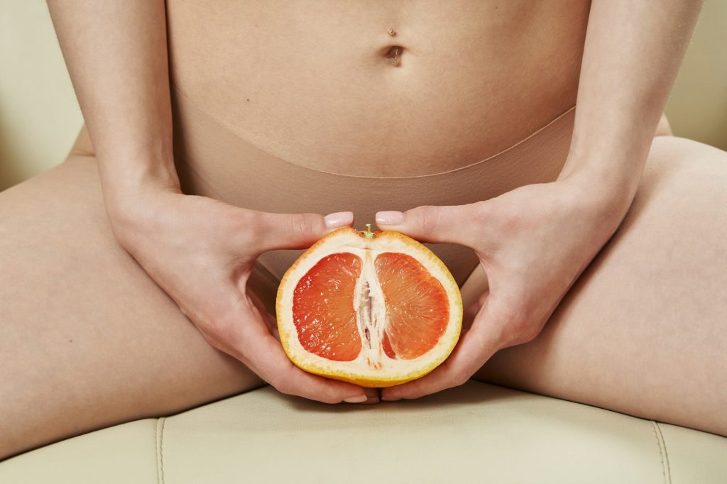 a beautiful slender female body and a cut half of a grapefruit between the legs. the concept of