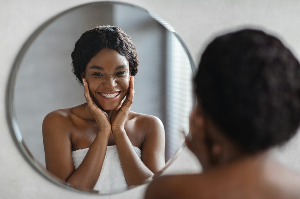 Mirror reflection of young black woman applying facial product
